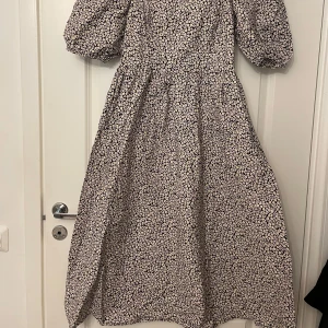 Blommig klänning med puffärmar - Supersöt blommig bomulls klänning med puffiga kortärmar och fyrkantig ringning. Klänningen har smock i ryggen och ett flowy fall som ger en romantisk känsla. Perfekt för vår och sommar! Passar storlek M-L bäst