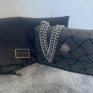 Svart axelväska med silverdetaljer från Kurt Geiger - Säljer en svart axelväska från Kurt Geiger med quiltat mönster och silverfärgade nitar. Perfekt för att styla upp en outfit 💕💕