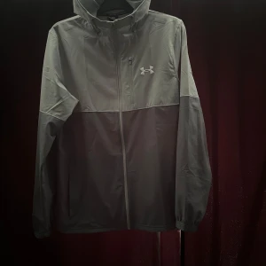 Mörkgrå träningsset från Under Armour - Snygga mörkgrå träningsbyxor med storlek XL från Under Armour med logga på låret. Byxorna har en sportig passform och resår i midjan, perfekta för gymmet eller löprundan. Jackan är från JD sports med storlek M 