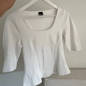 Topp - Säljer en stilren vit topp från Gina Tricot med rundad, djup ringning och trekvartsärmar. Toppen har en figurnära passform. 