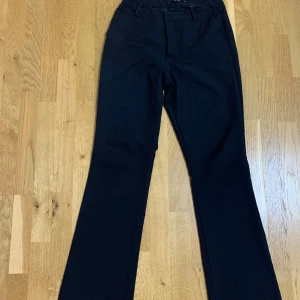 Svarta kostymbyxor från BikBok - Klassiska svarta kostymbyxor från BikBok i storlek 40. Byxorna har raka ben, hällor för bälte och diskreta fickor bak. Perfekta för en stilren och enkel look.