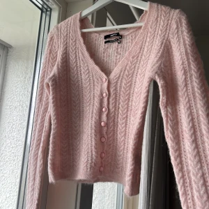 Ljusrosa kofta med knappar - Säljer en ljusrosa, fluffig kofta från Bik Bok med v-ringning och fina knappar framtill. Koftan har ett diskret mönster och är croppad i modellen. Perfekt att slänga på sig över en topp!