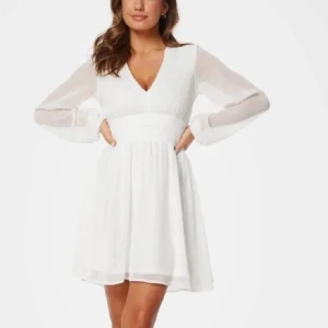 Vit klänning  - Superfin vit klänning med v-ringning, långa transparenta ärmar och markerad midja med knytband bak. Den har en liten fläck men syns knappt Kjolen är lätt utställd och slutar ovanför knäna. Perfekt för vår och sommar! Nypris 600