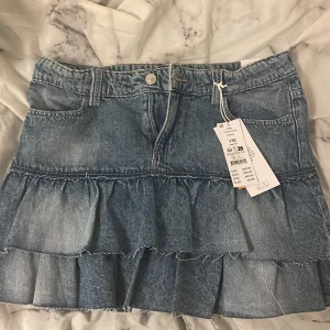 Jeanskjol med volanger från Gina tricot  - Säljer en blå jeanskjol med volanger från ginatricot. Kjolen har klassisk femficksdesign, knapp och dragkedja framtill samt volangdetaljer i två lager. Perfekt för dig som gillar en trendig och avslappnad stil. Den är helt ny❤️