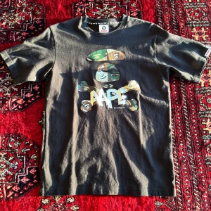 Svart t-shirt från Aape by A Bathing Ape/Bape - Säljer en svart t-shirt från Aape by A Bathing Ape med stort tryck framtill i camo och vitt. Klassisk passform med rund hals och korta ärmar. Aldrig använd BAPE tröja.