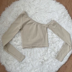 Beige croppad oneshoulder topp från STR - Säljer en beige croppad topp från STR med lång ärm och oneshoulder-design. Perfekt för dig som vill ha en stilren och trendig look. Toppens material känns mjukt och skönt mot huden. Storlek S enligt märket men passar bäst XS eftersom den är ganska tight vid armen.