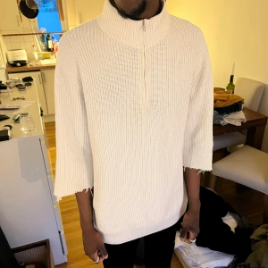 Vit stickad tröja med halv dragkedja - Säljer en vit stickad uniqlo tröja med hög krage och halv dragkedja framtill. Tröjan har trekvartsärmar med råa kanter och en avslappnad passform. Jag har klippt armarna.