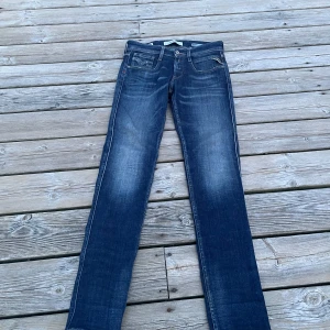 Blå Replay jeans  - Säljer ett par klassiska blå jeans från Replay med slim passform och snygga slitningar framtill. Jeansen har fem fickor, dragkedja och knapp i midjan samt detaljerade bakfickor. Tillverkade i hållbar bomull.