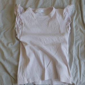 Ljusrosa ribbad topp med volangärmar från Gina Tricot - Supersöt ljusrosa ribbad topp från Gina Tricot med volangdetaljer på ärmarna. Ärmlös modell med romantisk känsla och rund halsringning. Perfekt för vår och sommar! Nyköpt!