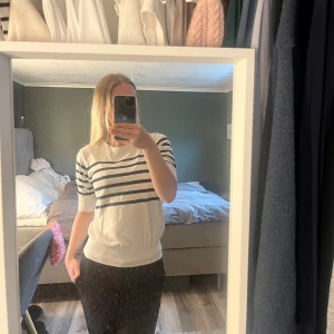 Vit t-shirt med marinblå ränder - Vit t-shirt med marinblå horisontella ränder över bröstet. Klassisk och enkel design med rund hals och korta ärmar. Perfekt för en avslappnad stil.