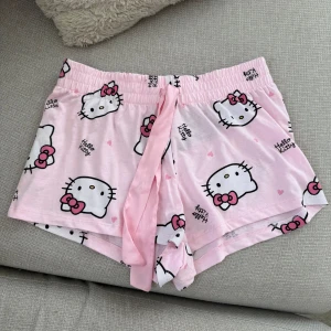 Hello Kitty shorts - Säljer ett par söta rosa shorts med Hello Kitty-motiv och små hjärtan. Perfekta för mysiga dagar hemma eller som pyjamasshorts. Oanvända med lapparna kvar.