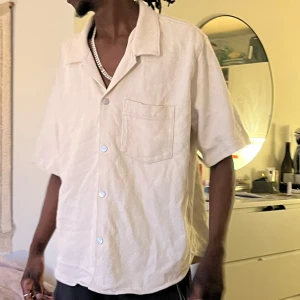 Beige kortärmad skjorta i manchester - Säljer en beige kortärmad skjorta i manchester med klassisk krage och bröstficka. Skjortan har knappar framtill och en avslappnad passform. Perfekt för dig som gillar en stilren och enkel look.