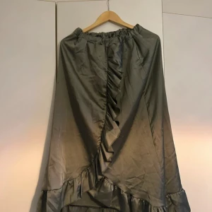 Grön långkjol med volang - Snygg grön långkjol med volangdetaljer och omlottkänsla. Kjolen har resår i midjan och ett elegant fall. Perfekt för dig som gillar en stilren men ändå unik look.