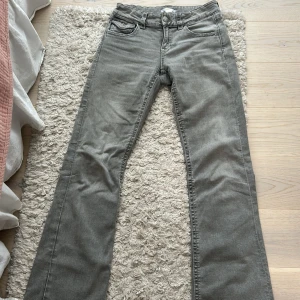 Grå bootcut jeans med broderade bakfickor - Säljer ett par grå bootcut jeans från Gina Tricot med snygga broderade detaljer på bakfickorna och silverfärgade knappar. Klassisk femficksmodell med normal passform och låg midja. Bra i passformen 