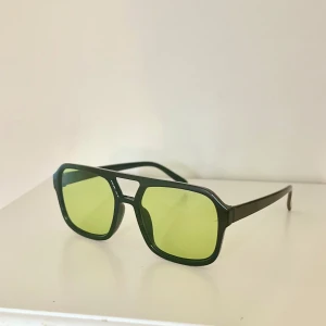 Svarta solglasögon med gröna glas - Snygga svarta solglasögon med rektangulära, gula glas och bred båge. Klassisk modell med modern touch som passar perfekt för att sticka ut🤵🏼 Glasögonen har en markerad näsbrygga och raka skalmar😎