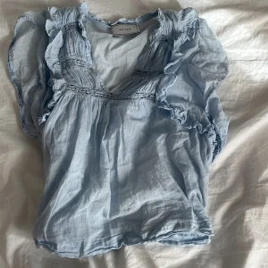 Ljusblå volangblus från Neo Noir - Supersöt ljusblå blus från Neo Noir med volangdetaljer längs ärmar och halsringning. Perfekt nu till sommaren💕Säljer då den är för stor och är bara använd ett fåtal gånger