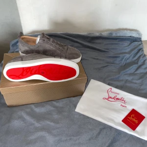 Gråa Loubs utan spikar - Säljer ett par exklusiva gråa sneakers från Christian Louboutin med klassisk röd sula. Skorna är i mocka med snörning och har en vit platt sula. Perfekta för dig som vill sticka ut med stilrena detaljer och lyxig känsla. ❇️Sprillans nya❇️, ❇️Helt oanvända❇️