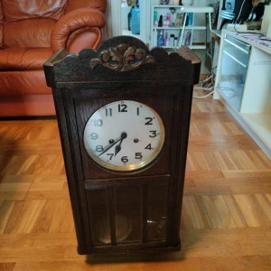 Antik väggklocka i mörkt trä - En vacker antik väggklocka med detaljerad trädesign. Perfekt för att lägga till en vintage touch till ditt hem. Klockan har en klassisk urtavla med tydliga siffror och visare. Denna väggklocka är ett charmigt tillskott till alla rum och en fantastisk inredningsdetalj. ..funkae ej men om Man är händig så kan man nog få igång den..Gammal och fin väggklocka  Höjd 62 Bredd 31 Osäker om den går rätt men går när man drar upp den