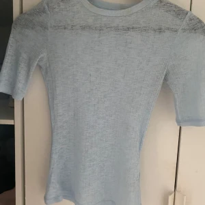 Ljusblå transparent topp - Säljer en ljusblå, tunn och transparent topp med korta ärmar. Perfekt att styla med ett linne under eller som layering-piece. Materialet är lätt och stretchigt, vilket gör den bekväm att bära.