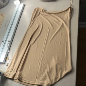 Beige kortklänning från Jeff Gallano - Säljer en stilren beige kortklänning från Jeff Gallano. Klänningen har en enkel design med smala axelband och är tillverkad i ett mjukt, slätt material som ger en snygg passform. Perfekt för dig som gillar minimalistisk stil.