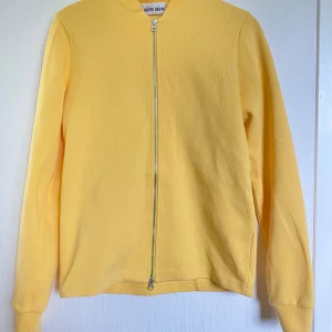Gul zip-jacka från Séfr - Säljer en ljusgul jacka från Séfr i 100% bomull. Jackan har lång ärm och hel dragkedja framtill. Enkel och stilren design utan synliga fickor eller mönster. Perfekt för dig som gillar färg och minimalistisk stil.
