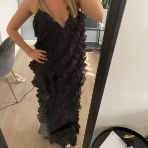 Svart långklänning med volanger - Säljer en svart långklänning med djup v-ringning och massor av volanger som ger en riktigt snygg och dramatisk look. Perfekt för dig som vill sticka ut på festen! Klänningen är ärmlös och har en elegant siluett. Det är något insydd för att få en mer figursydd look. Jag bär vanligtvis storlek 36 eller mindre. Kan mötas i Stockholm om man vill testa innan köp. Endast använd en gång på min bal för 2 år sedan.