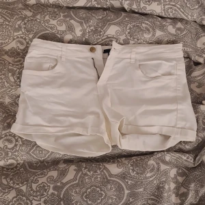 Vita shorts från H&M - Säljer ett par vita shorts från H&M i storlek 38. De har klassisk femficksdesign, knapp och dragkedja framtill samt uppvikta benslut. Perfekta för varma dagar och enkla att matcha med olika toppar.