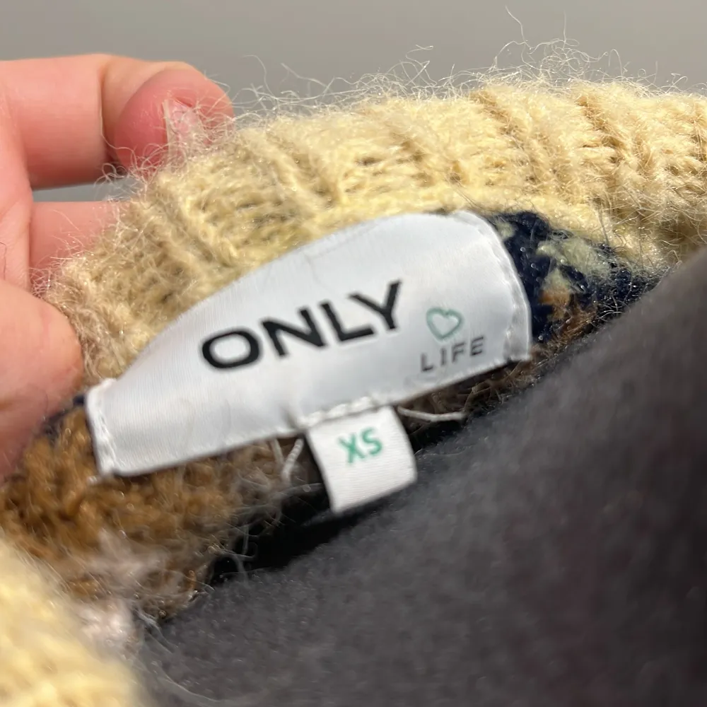Säljer en mysig stickad tröja från ONLY i storlek XS. Tröjan har ett färgglatt mönster i beige, brun, grön och vit med långa utsvängda ärmar och rund hals. Perfekt för kyliga dagar!💚🤎💛🤍. Neuletakit & Villapaidat.