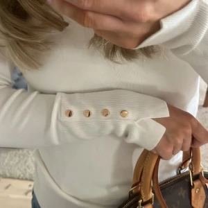 Vit långärmad tröja med knappar - Säljer en stilren vit långärmad tröja med dekorativa guldknappar vid ärmsluten. Tröjan har en normal passform och är tillverkad i ett mjukt material som ger en bekväm känsla. Perfekt för en elegant vardagslook💖💖 Stl S