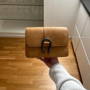 Väska - Snygg beige axelväska med en unik hästskospänne framtill. Köpt för över fem år sedan men knappt använd🤍 som ny