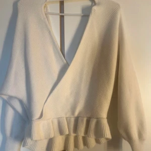 Vit långärmad tröja  - Säljer en stilren vit omlottstickad tröja med volangdetaljer i nederkant. Tröjan har långa ärmar och en djup v-ringning, perfekt för en elegant look.