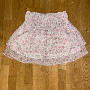 Blommig kjol - Söt blommig kortkjol. Kjolen har en volangdetalj och är perfekt för sommarens varma dagar. Den elastiska midjan ger en bekväm passform. Skulle säga att den också sitter som en xs pågrund av att det är elastiskt band. Väldigt bra skick eftersom den är använd max fem gånger! Hör av dig vid frågor, finns kvar tills den är markerad såld🥰