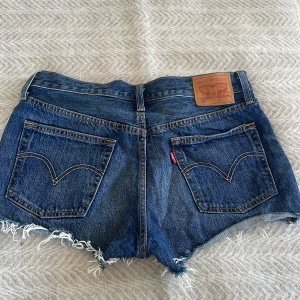 Blå jeansshorts från Levi's - Säljer ett par klassiska blå jeansshorts från Levi's med fransiga kanter och femficksdesign. Shortsen har en knappgylf och är perfekta för en avslappnad stil. Passar utmärkt till sommardagar! 💙