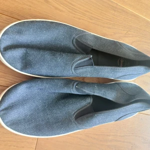 Blå loafers i jeansmaterial - Snygga blå loafers i jeansmaterial med vit sula och en brun detalj vid hälen. Perfekta för en avslappnad stil och enkla att matcha med olika outfits.
