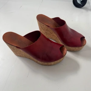 Röda kilklackar i skinn - Snygga röda kilklackar från Robert Clergerie i skinn med korksula. Dessa slip-in skor har en öppen tå och en hög kilklack som ger extra höjd och stil. Perfekta för sommarens alla tillfällen.