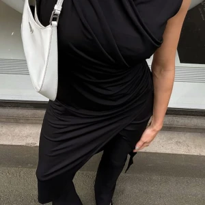 Svart klänning från NA-KD - Snygg svart klänning från NA-KD med omlott-design och ärmlös stil. Perfekt för en elegant look. Klänningen har en draperad effekt som ger en smickrande passform. Köpt för 350kr