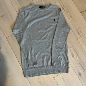 Grå tröja från Polo Ralph Lauren - Säljer en stilren grå tröja från Polo Ralph Lauren med rund hals och broderad logotyp på bröstet. Tröjan har långa ärmar och ribbade muddar vid ärmslut och nederkant. Perfekt för en avslappnad look.Snygg och stilig ralph lauren tröja i fint skick, måtten ser ni, fraktar inom 24h, skriv vid funderingar👍🏻