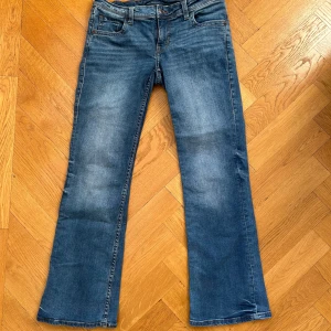 Lågmidjade bootcut jeans med snygga fickor - Snygga lågmidjade blå bootcut jeans med knappdetalj på bakfickan från HM Divided. Lite slitage längst ner på bägge benen, se bild 4 & 5