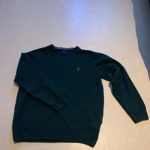 Grön ulltröja från GANT - Säljer en stilren grön tröja från GANT i superfin lammull. Tröjan har en klassisk design med rund hals och långa ärmar. Perfekt för kyligare dagar. Passar både till jeans och chinos.