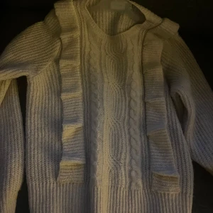 Vit stickad tröja från VILA - Säljer en vit stickad tröja från VILA med kabelstickat mönster och volangdetaljer på framsidan. Nästan aldrig använd 