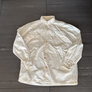 Vit overshirt från Zara - Säljer en stilren vit overshirt från Zara. Skjortan har två bröstfickor med knappar och en klassisk krage. Perfekt för en avslappnad men ändå uppklädd look. Bra för vår och försommar. Stor passform, passar M