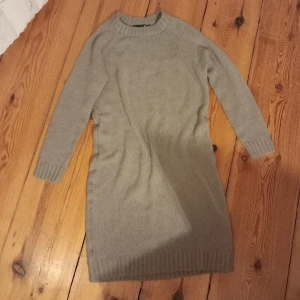Beige stickad klänning från 157 - Säljer en mysig beige stickad klänning från 157. Klänningen har långa ärmar och en rund halsringning. Perfekt för kyligare dagar och kan enkelt stylas med olika accessoarer. 100cm lång. 