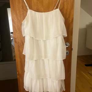 Vit klänning med volanger - Säljer en söt vit klänning med flera lager av volanger. Klänningen är med smala axelband och har en luftig passform. Perfekt för sommarens varma dagar!