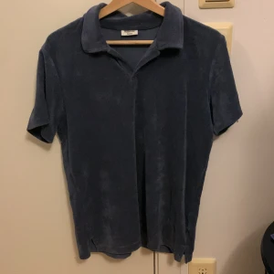 Mörkblå frotté t-shirt från Kappahl - Säljer en mörkblå frotté t-shirt från Kappahl. Den har en klassisk krage och korta ärmar, perfekt för en avslappnad stil. Materialet är mjukt och bekvämt, vilket gör den idealisk för varma dagar. Knappt använd bra sommar tröja