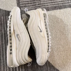 Vita Nike Air Max 97 sneakers - Snygga vita Nike Air Max 97 sneakers med den ikoniska vågiga designen och synlig Air-enhet i sulan. Skorna har en stilren look med snörning och diskreta Nike-loggor på sidan. Perfekta för en sportig och modern stil. Köpta på zalando använda lite men är i dunder skick fråga om du har minsta fundering😉
