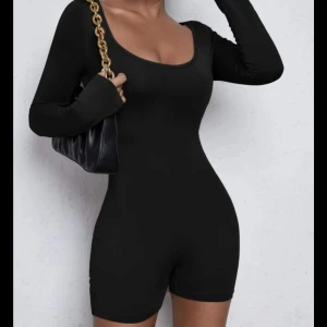 Svart långärmad jumpsuit - Snygg och stilren svart jumpsuit med långa ärmar och en tight passform. Perfekt för en kväll ute eller en avslappnad dag. Den har en rundad halsringning och är gjord i ett mjukt och stretchigt material.