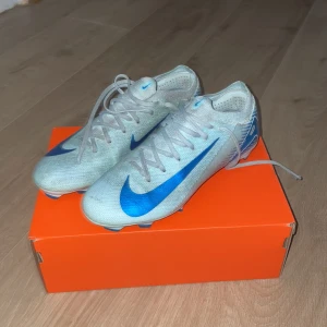 Nike fotbollsskor med blå detaljer - Snygga fotbollsskor från Nike i en ljus färg med blå detaljer. Skorna har snörning och är designade för att ge bra grepp på planen. Perfekta för fotbollsträning och matcher. Skriv till mig för diskussion för pris!