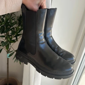 Svarta boots - Snygga svarta boots i skinn med en robust sula. De har en klassisk design utan snörning och är perfekta för både vardag och mer uppklädda tillfällen.
