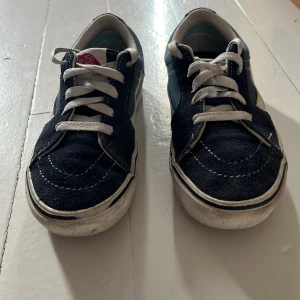 Blå och vita sneakers från Vans - Säljer ett par klassiska Vans sneakers i blått och vitt. Skorna har en snygg design med vita snören och den ikoniska Vans-loggan på hälen. Perfekta för en avslappnad stil.