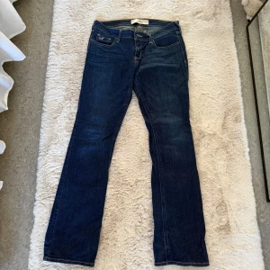 Mörkblå jeans från Hollister - Snygga mörkblå jeans från Hollister med klassisk femficksdesign och broderade bakfickor. De har en knapp- och dragkedjestängning samt bälteshällor. Perfekta för en avslappnad stil. Säljer dom då dom ej används